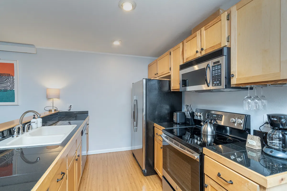 A well-equipped kitchen with black appliances, warm wooden cabinetry, a granite countertop, and decorative wall art. The space is ideal for cooking, entertaining, or enjoying a morning coffee.