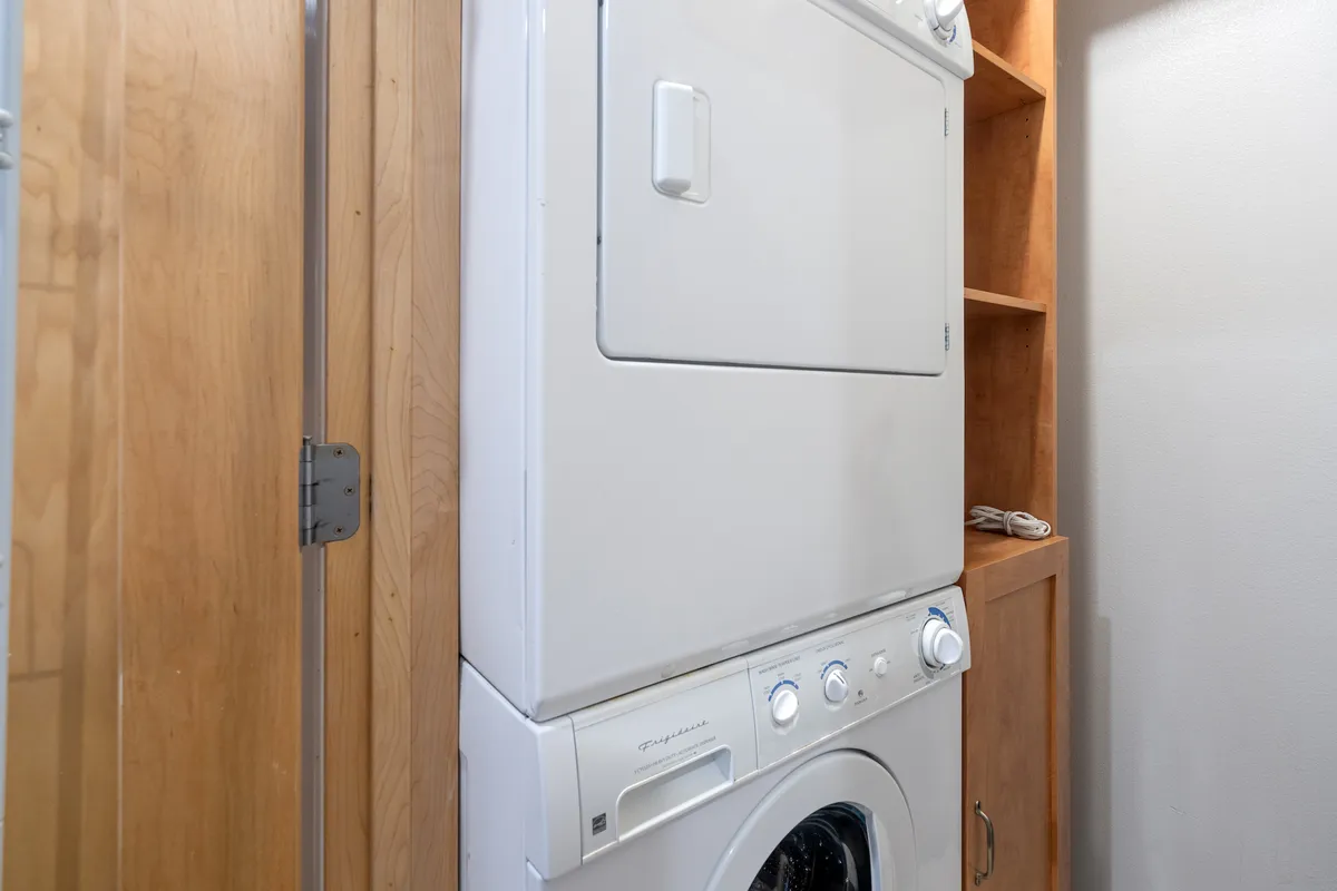A close-up of a practical laundry nook with a stacked washer and dryer set against wooden shelving. The area is clean, organized, and easily accessible, illustrating the convenience of handling laundry needs without leaving the comfort of the home.