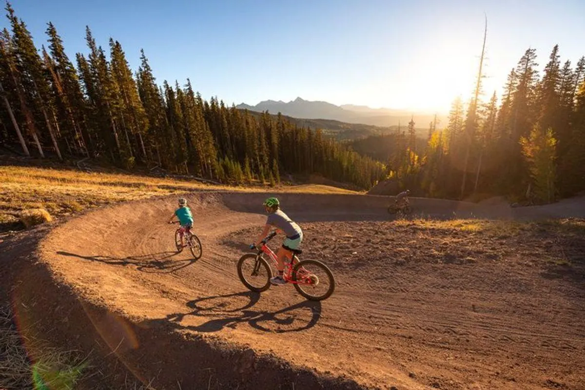 Bicyclists ride along a scenic curved trail framed by mountains and open landscape, exuding energy and a sense of outdoor freedom. The trail is wide and accessible, ideal for nature walks or family exploration.