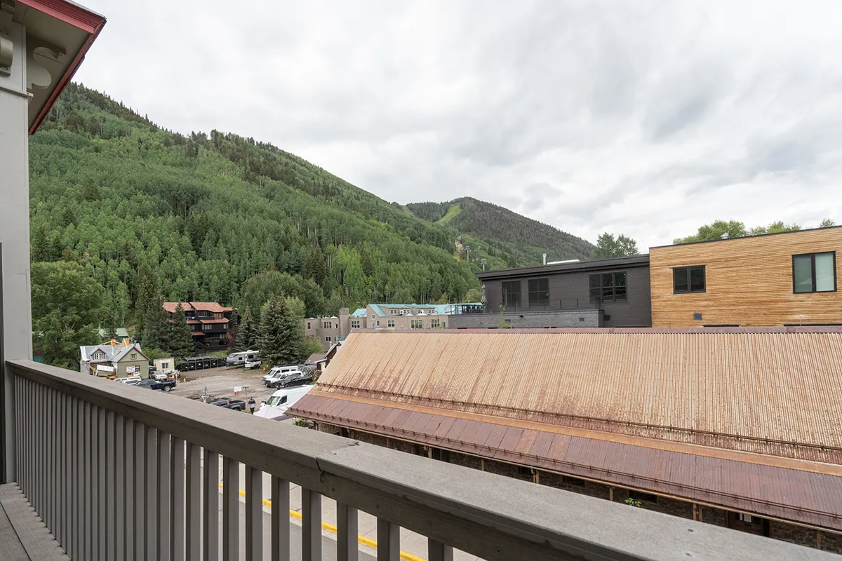 A tranquil scene featuring a mountainous landscape with wooden buildings along an asphalt road under a cloudy sky. The village feel is palpable, suggesting proximity to local conveniences and scenic surroundings.