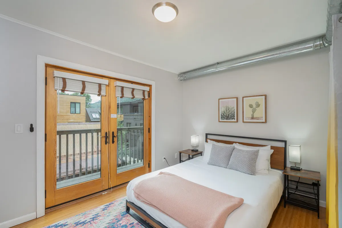 A cozy guest bedroom with a queen bed, stylish artwork above the headboard, and French doors that let in abundant natural light. The room feels intimate and warm, ideal for guests or family members seeking their own comfortable space.