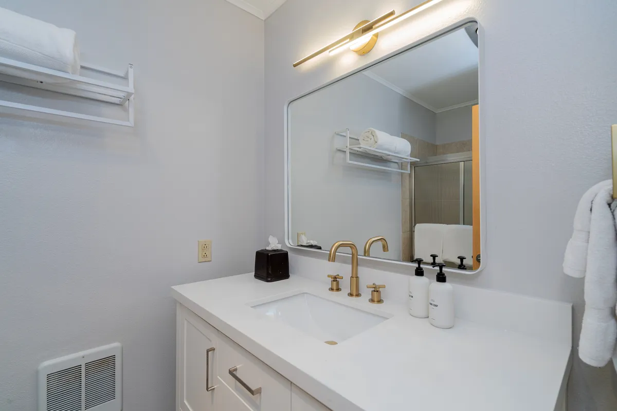 A tranquil bathroom scene with a well-lit sink, mirror, and attractive lighting fixture. The ambiance is calm, offering a sense of relaxation and readiness for guests’ daily routines.